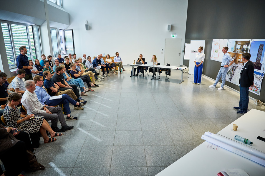 Matthias Eisele intervenes in the expert tribune. Beda Weber, Head of Timber Construction a.i. Implenia, listens intently.